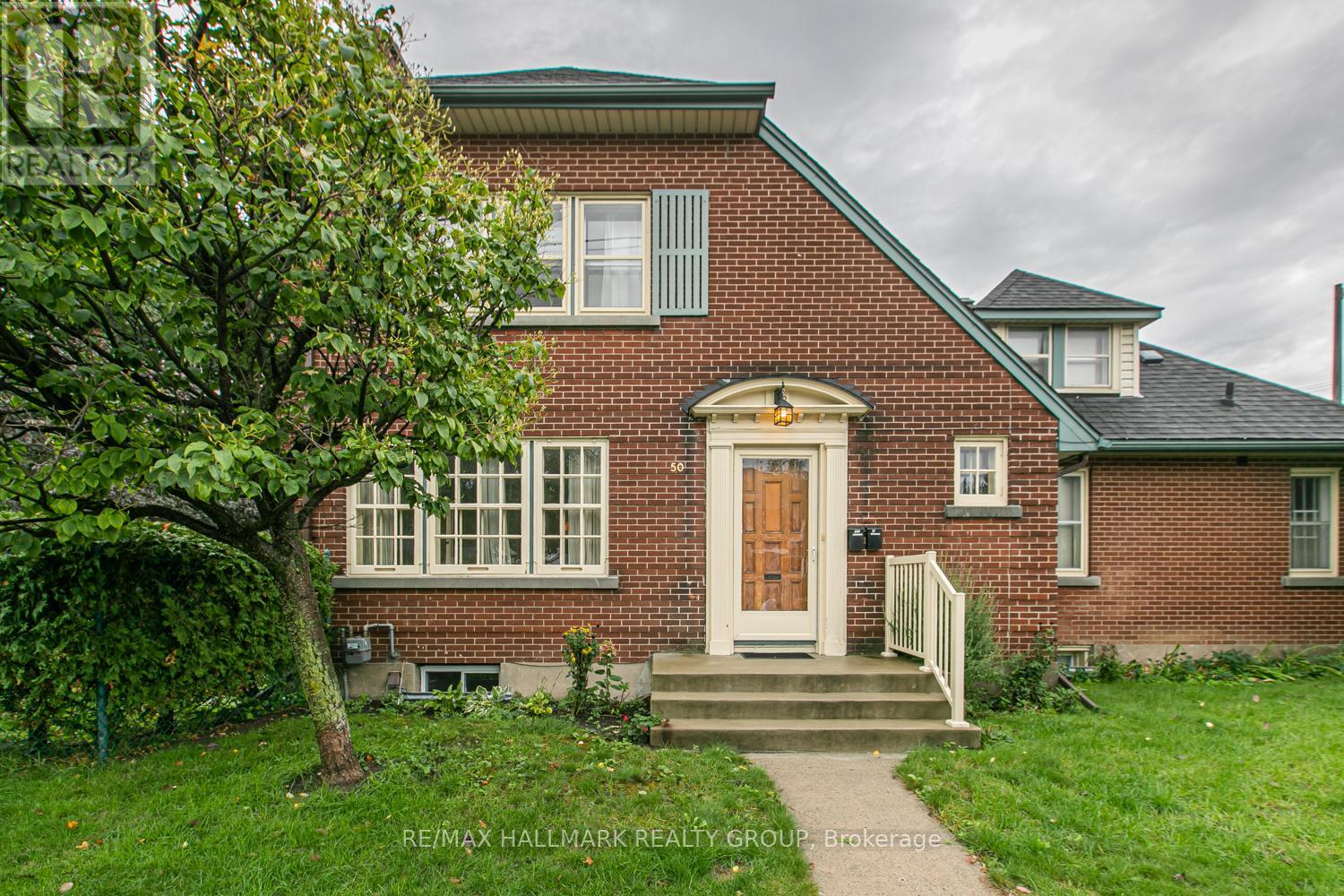 A red brick house with a white door and a tree in front.