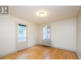 A room with a wooden floor, a window with white curtains, and a white door.