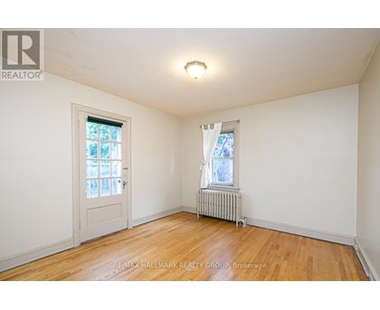 A room with a wooden floor, a window with white curtains, and a white door.