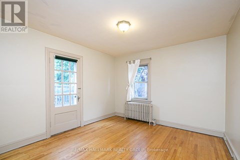 A room with a wooden floor, a window with white curtains, and a white door.