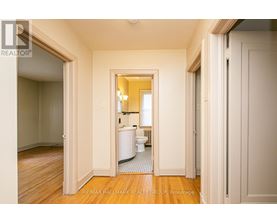 A hallway with a toilet and sink visible through the door.