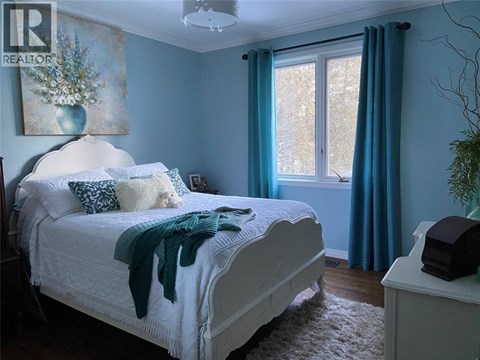 A bedroom with a white bed and a painting on the wall.