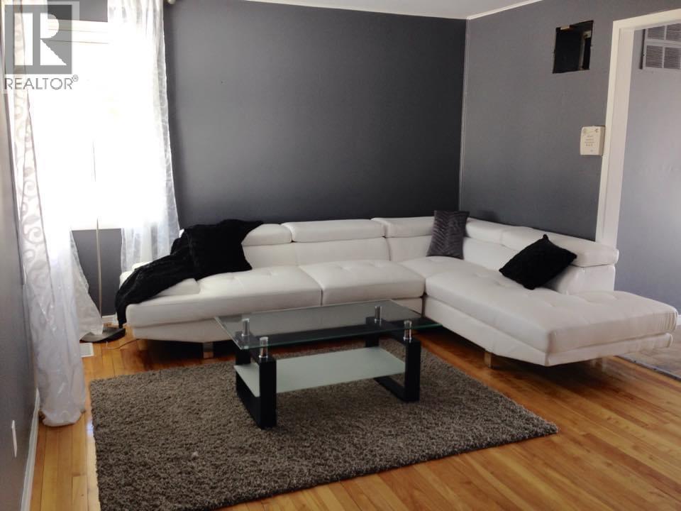 A white couch with a black pillow is in front of a grey wall.