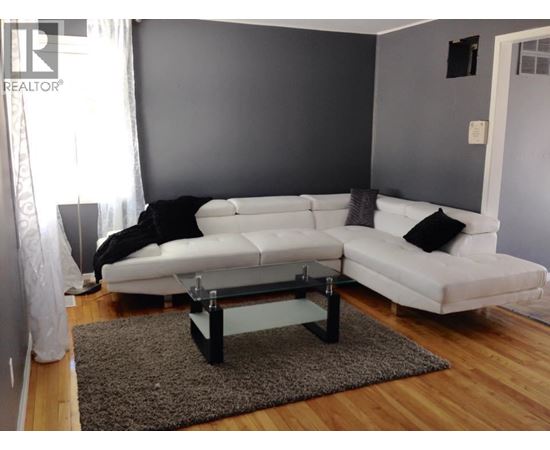 A white couch with a black pillow is in front of a grey wall.