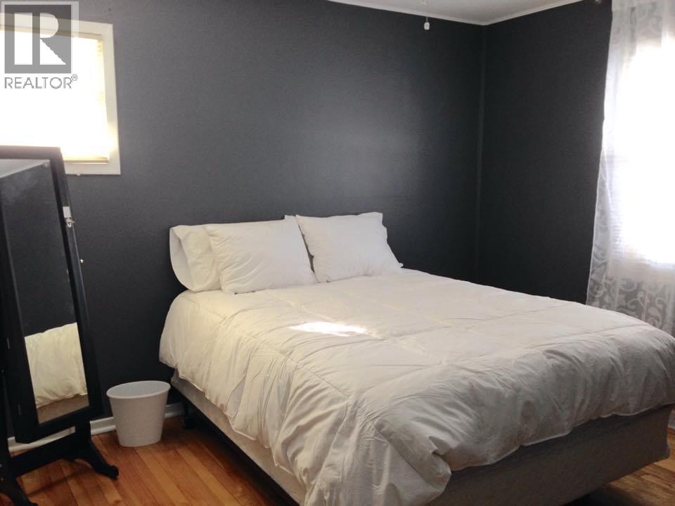 A bed with white sheets and pillows in a room with a wooden floor.