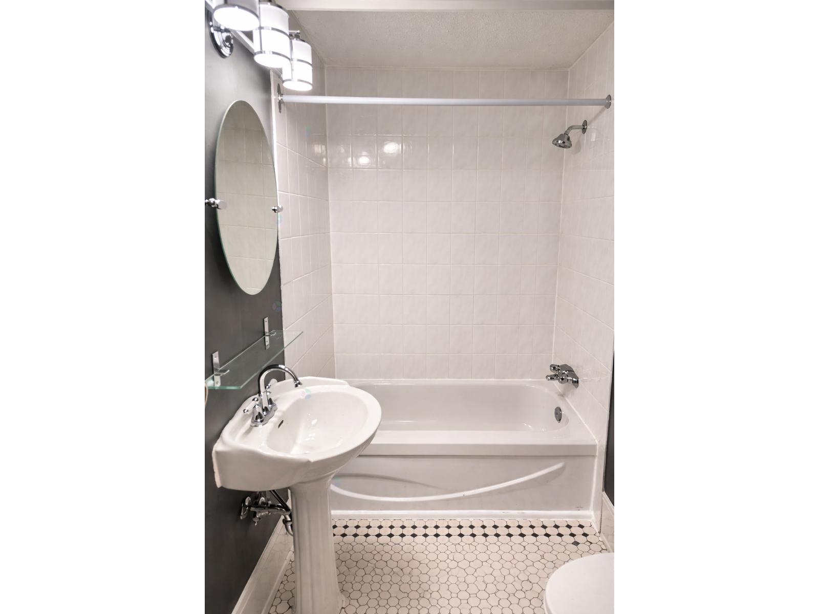 A white bathroom with a sink, mirror, and bathtub.