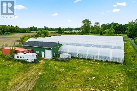 A greenhouse and a red building are situated in a grassy field.