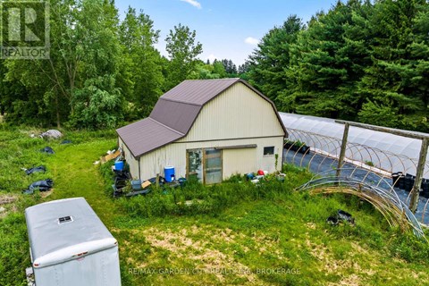 A small white building with a brown roof is surrounded by greenery.
