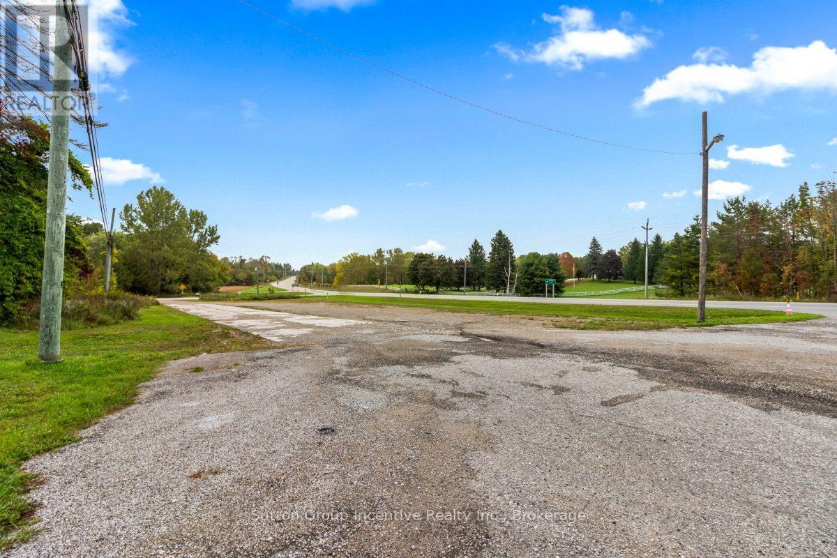 A gravel road leads to a grassy area with trees in the distance.