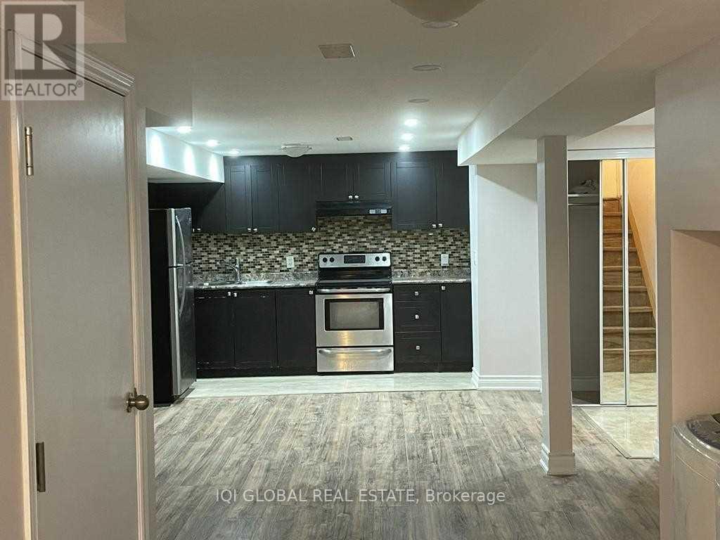 A kitchen with black cabinets and a patterned backsplash is visible from a hallway.