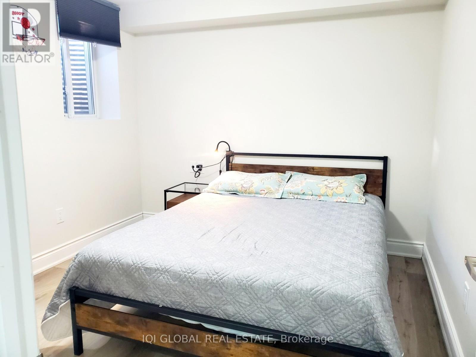 A bed with a wooden headboard and a grey bedspread is in a room with white walls.