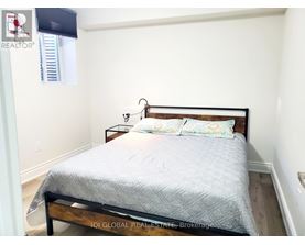 A bed with a wooden headboard and a grey bedspread is in a room with white walls.