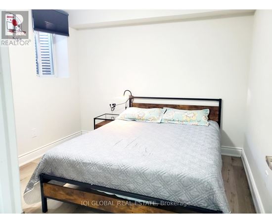 A bed with a wooden headboard and a grey bedspread is in a room with white walls.