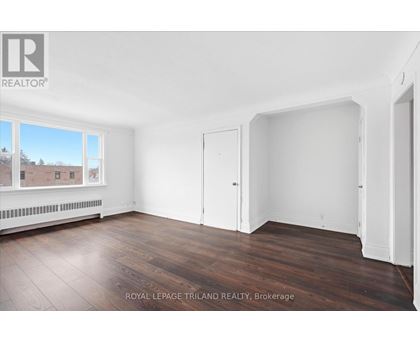 A room with white walls and wooden flooring, with a window showing a view of a building and trees.
