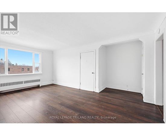 A room with white walls and wooden flooring, with a window showing a view of a building and trees.