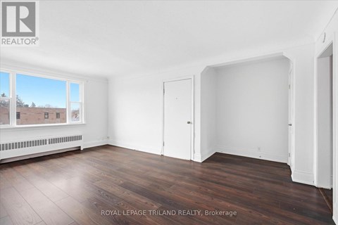 A room with white walls and wooden flooring, with a window showing a view of a building and trees.