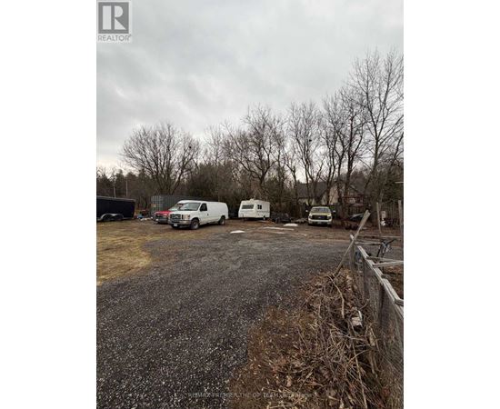 A gravel lot with a fence and a few parked vehicles.