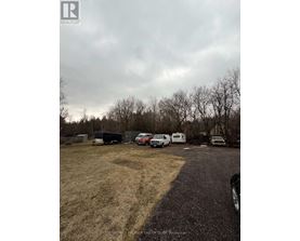 A realtor photo of a property with a gravel driveway, a few vehicles, and a fence.