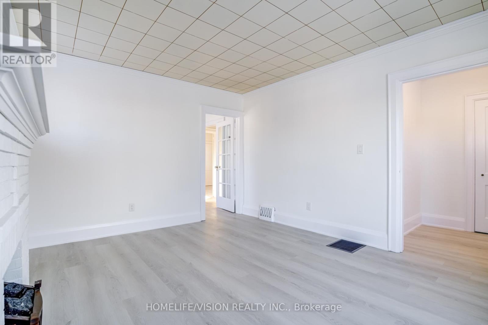 A spacious room with a white ceiling and light wood flooring.