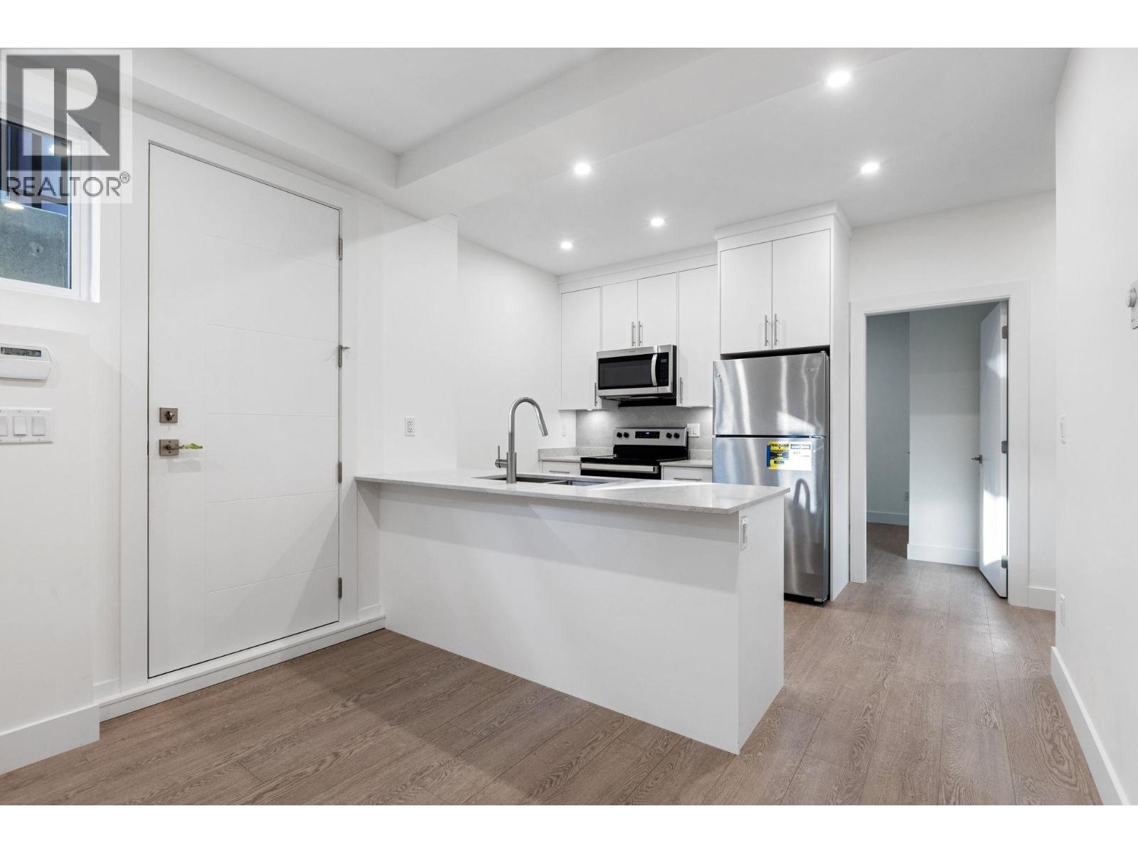 A modern kitchen with white cabinets and a wooden floor.
