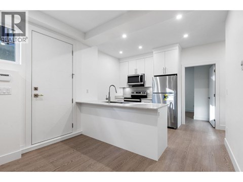 A modern kitchen with white cabinets and a wooden floor.