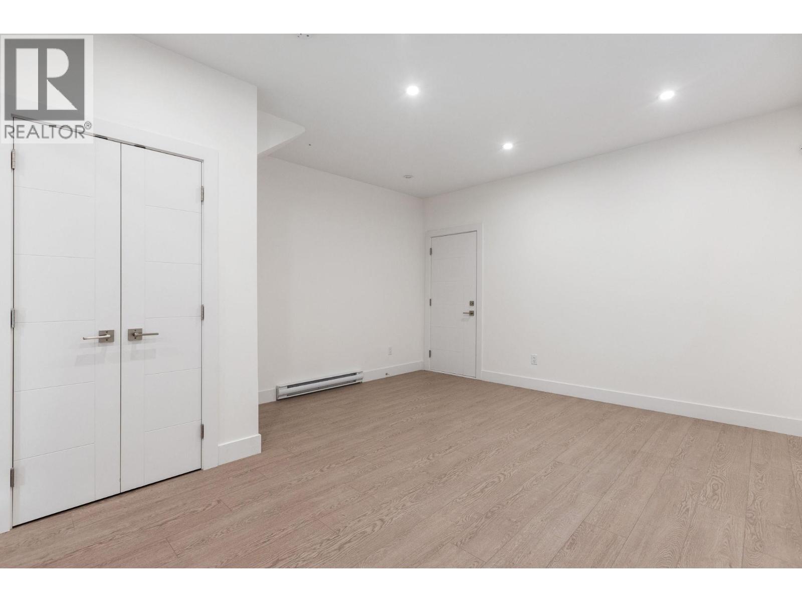 A room with a white wall and a wooden floor with a white door on the left and a white closet door on the right.