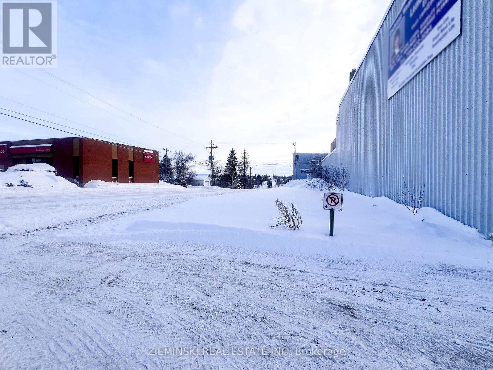 A snow-covered ground with a no parking sign in the foreground.