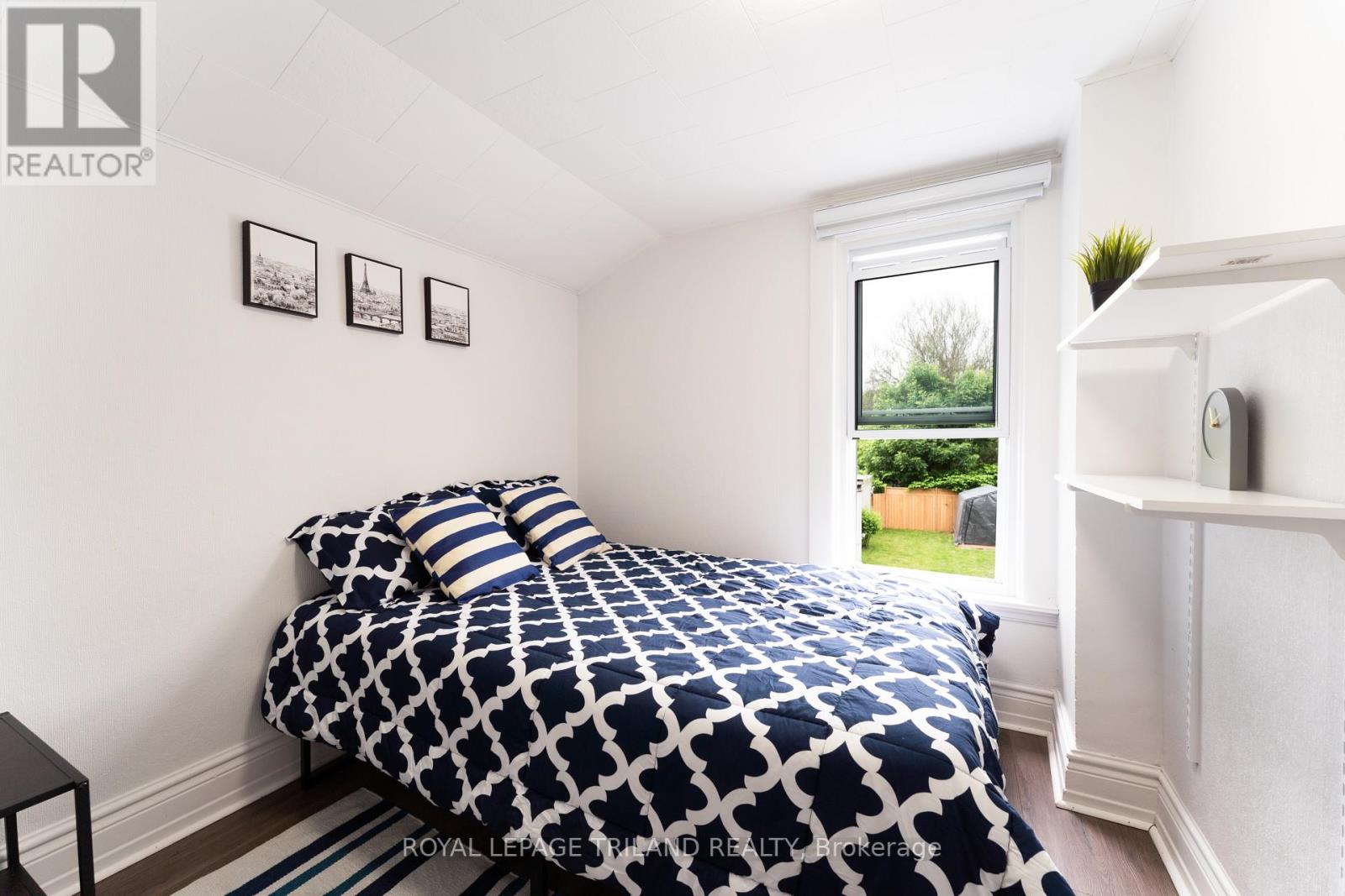 A bedroom with a patterned bedspread and a window showing a green outdoor area.
