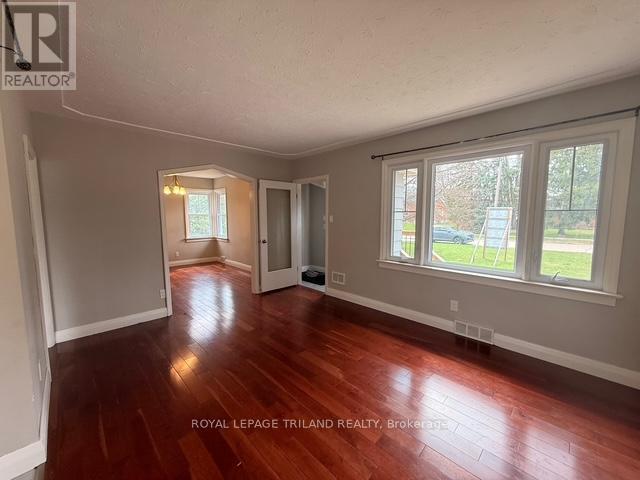 A room with wooden floors and white walls, with a window showing a view of a street.