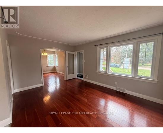 A room with wooden floors and white walls, with a window showing a view of a street.