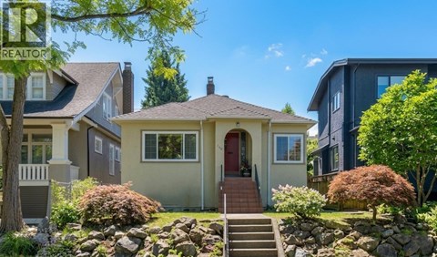 A house with a red door is surrounded by greenery and other houses.
