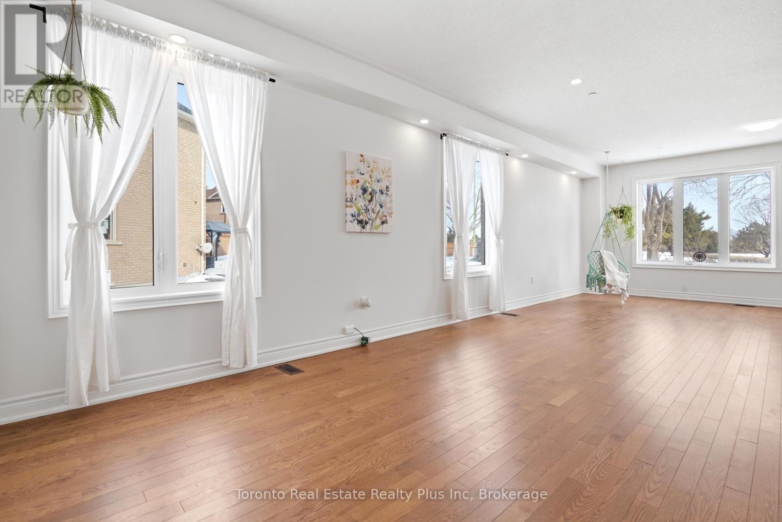 A spacious room with wooden floors and white curtains.