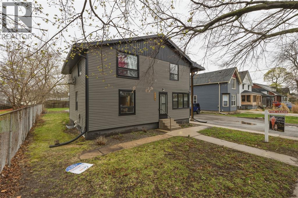 A house with a grey exterior is surrounded by a fence and has a tree in front of it.