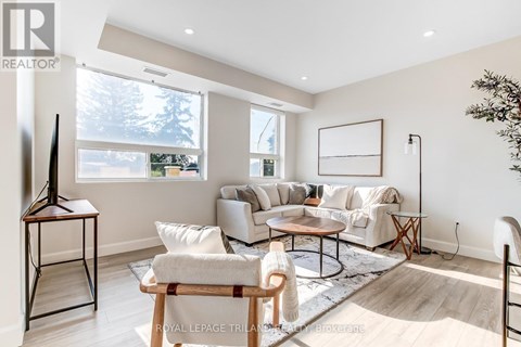 A living room with a white sofa set, a wooden coffee table, and a large window.