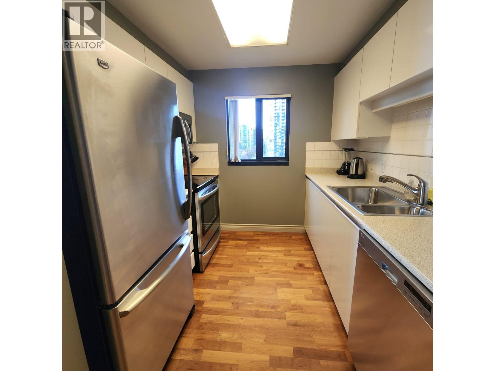 A kitchen with a stainless steel refrigerator and wooden flooring.