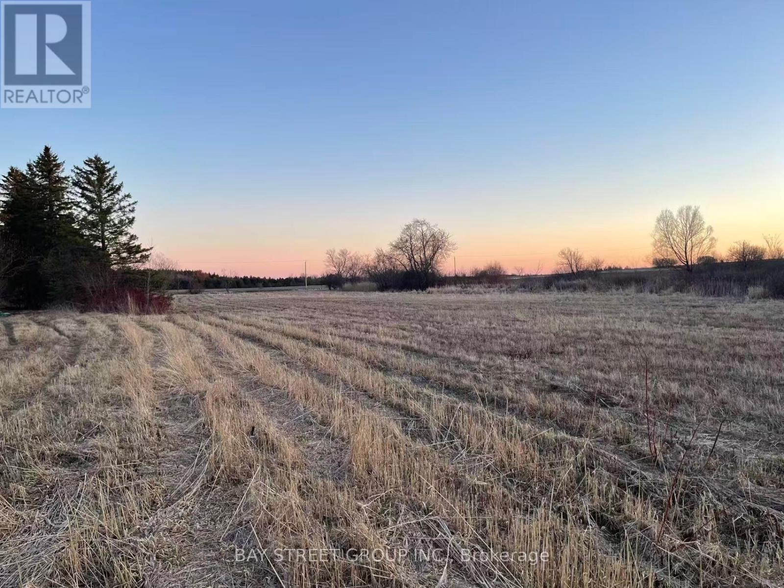 A field with a tree and a REALTOR sign in the corner.