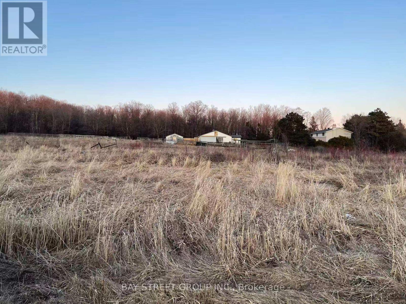 A field with dry grass and a few buildings in the distance.