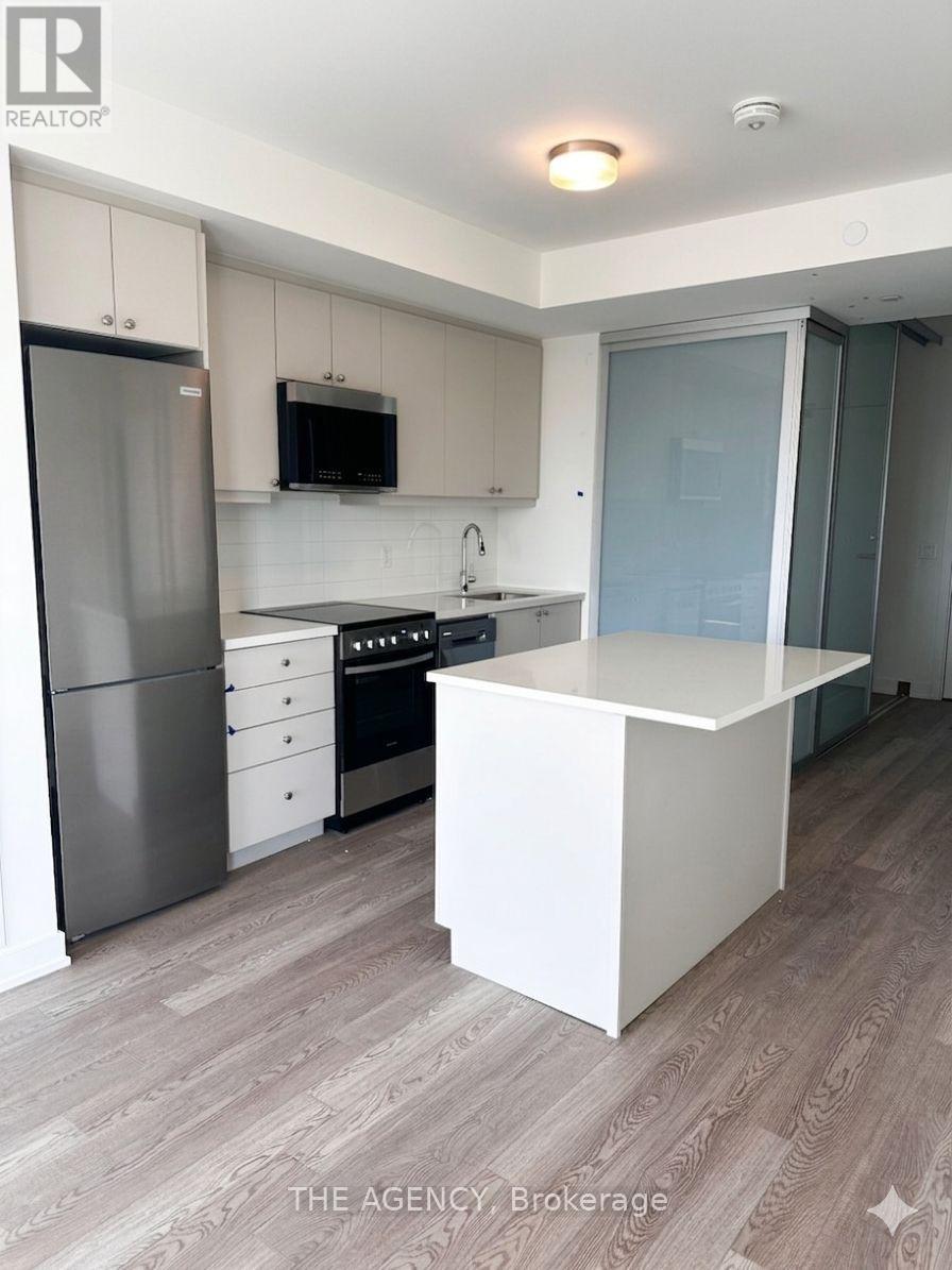 A kitchen with a refrigerator, microwave, oven, and sink.