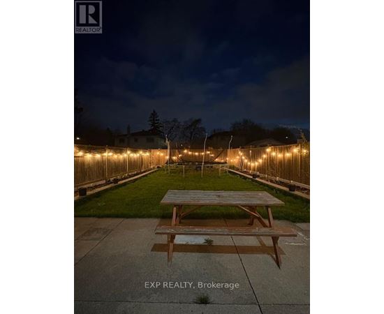 A picnic table is in the middle of a yard with lights on the fence.