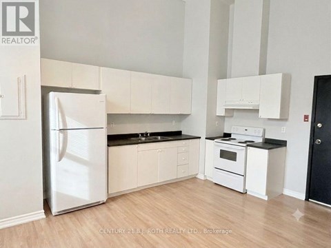 A white refrigerator stands in a kitchen with white cabinets and a black stove.