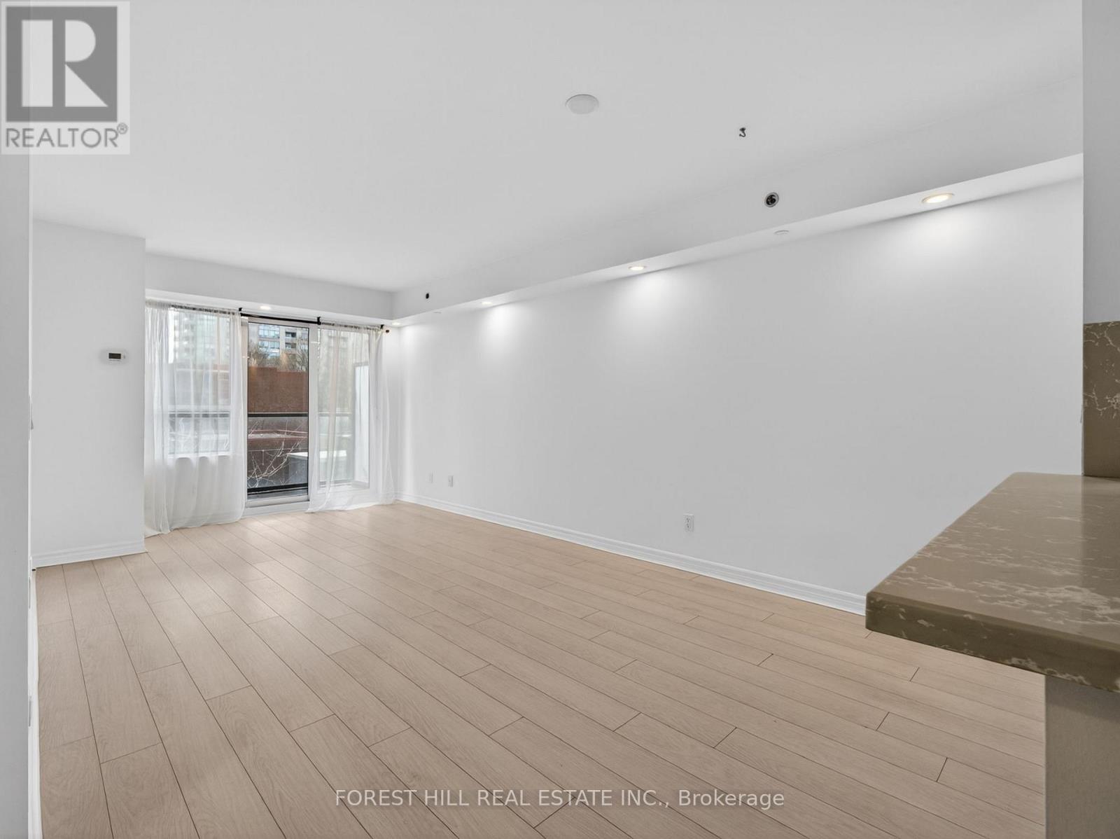 A spacious room with wooden flooring and a large window with curtains.