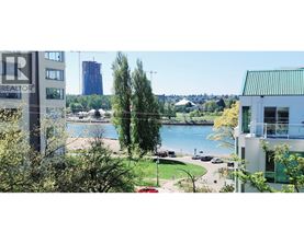 A realtor sign is in the foreground of a cityscape with a lake and greenery in the background.