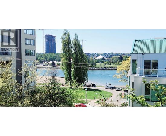 A realtor sign is in the foreground of a cityscape with a lake and greenery in the background.