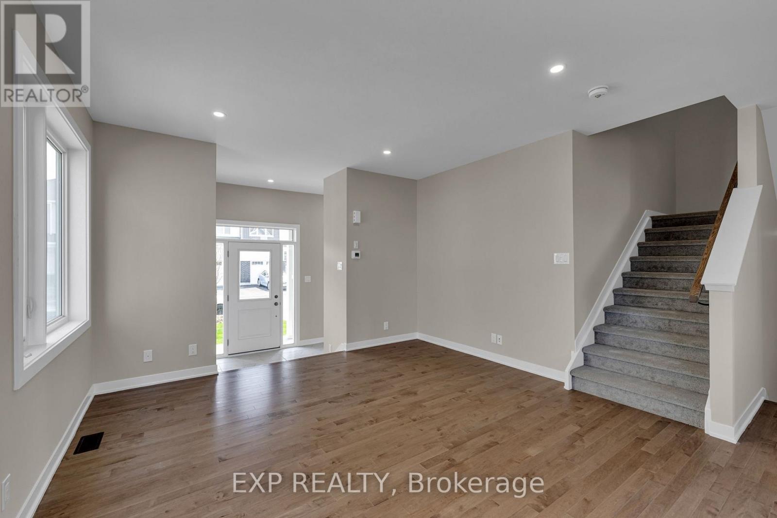 A spacious room with wooden floors and a staircase leading to another level.