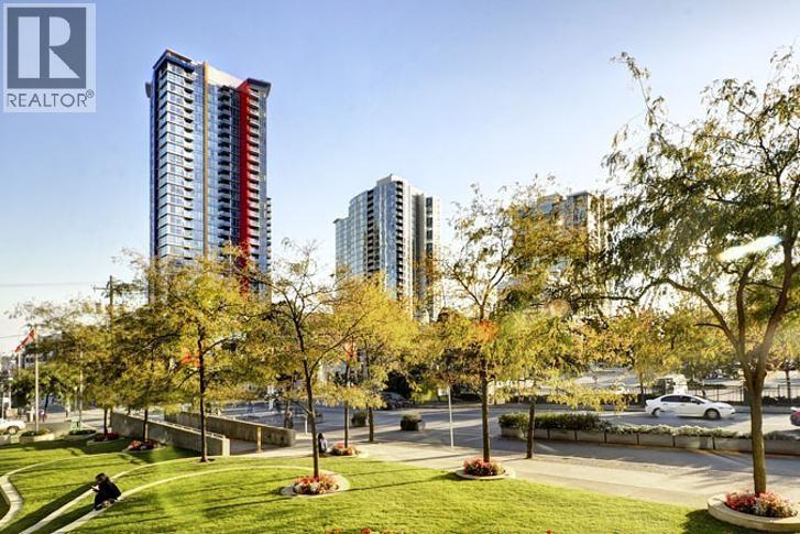 A city park with a grassy area and trees in the foreground with buildings in the background.