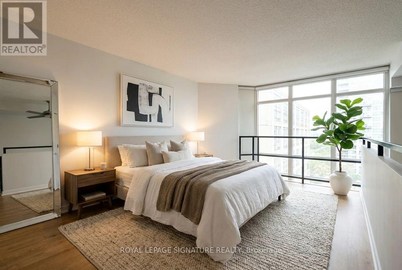 A bedroom with a large bed, a nightstand with a lamp, and a framed picture on the wall.