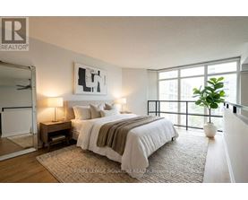 A bedroom with a large bed, a nightstand with a lamp, and a framed picture on the wall.