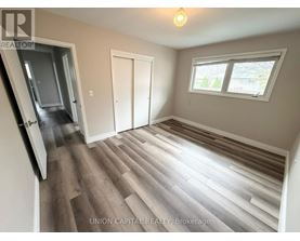 A room with wood flooring and a window with a view of trees outside.