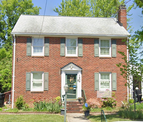 A red brick house with a white door and green shutters.