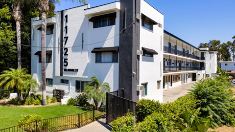 A white building with black numbers on the side and a black fence in front.